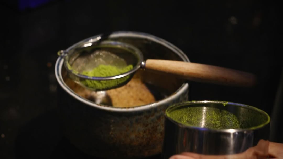 Matcha powder being sifted in preparation for a matcha latte